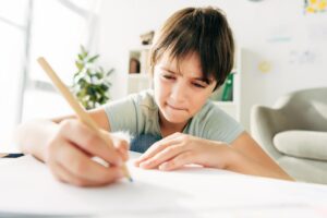 kid with dyslexia drawing with pencil and sitting at table